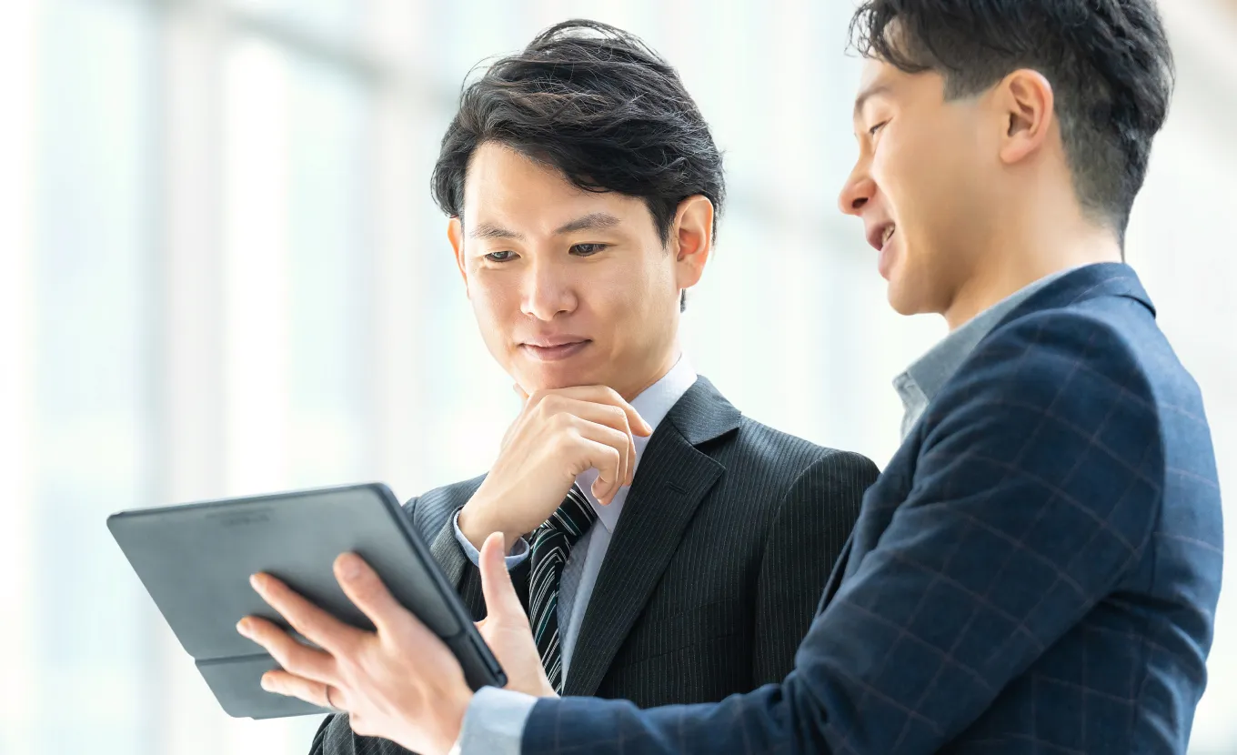 タブレットを見ながら話すスーツ姿の二人