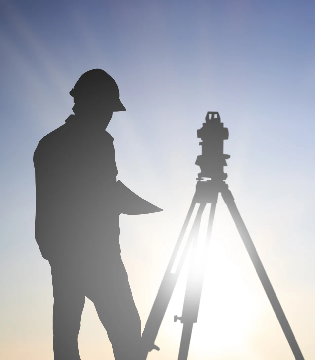 夕日を背に測量機器を操作する作業員のシルエット