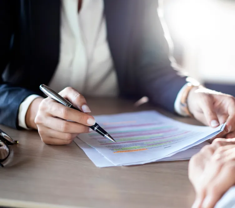 机の上の資料を指しながら説明するビジネスパーソンの手元