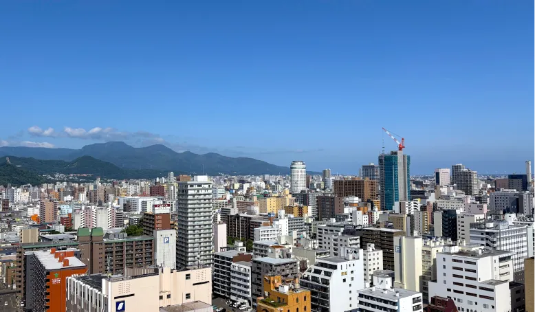 青空の下に高層ビルと山並みが広がる都市景観