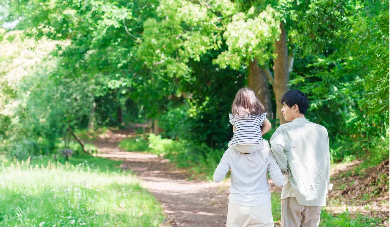 緑の木々に囲まれた小道を歩く家族の後ろ姿